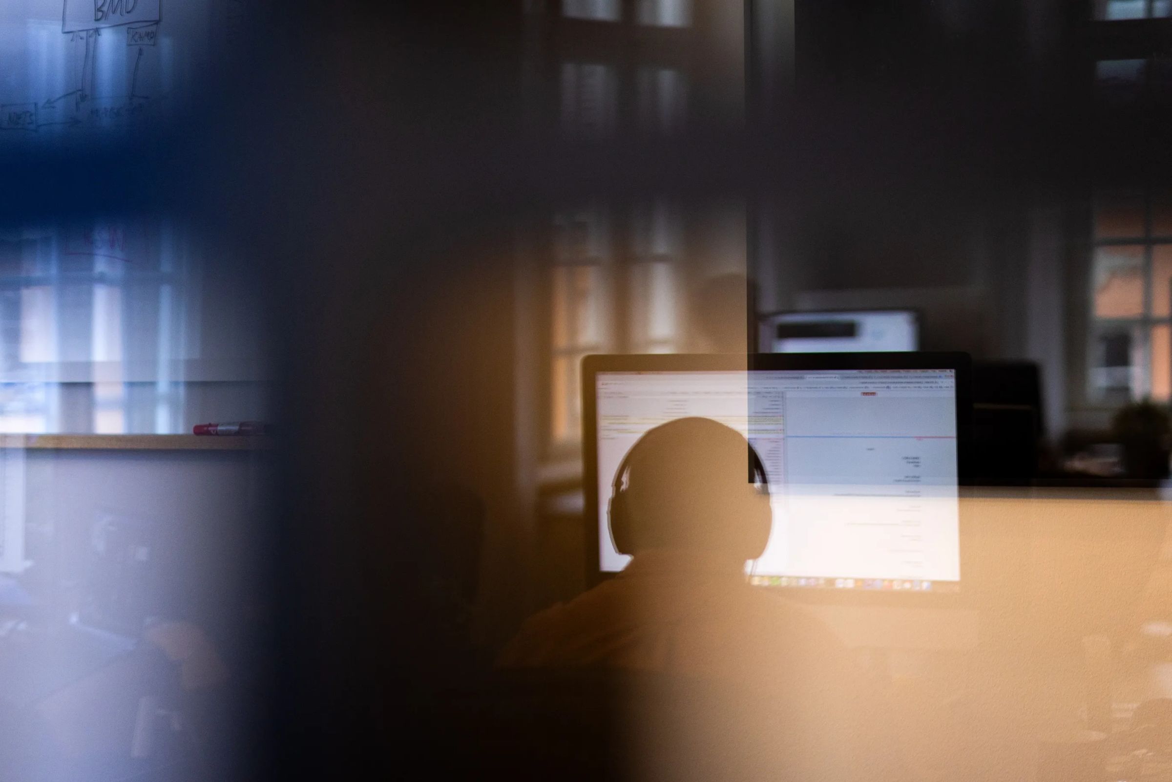 Silhouette of a person wearing headphones, working at a computer in a dimly lit office