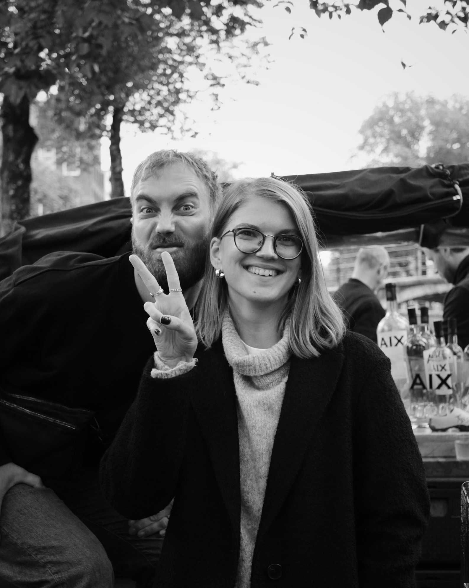 Svartvitt foto av två kollegor utomhus, den ena gör ett V-tecken och den andra en grimas