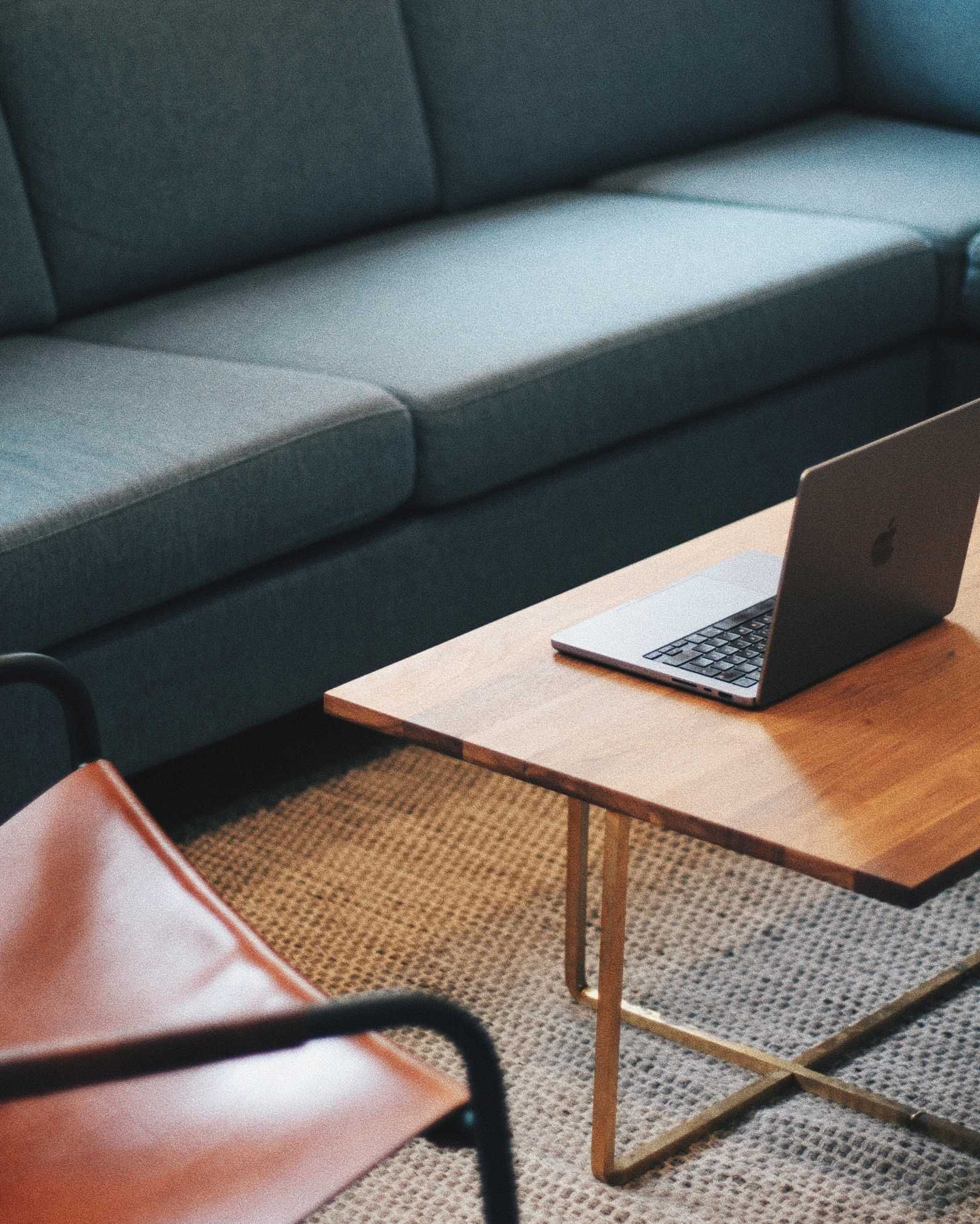 Laptop on a wooden coffee table in front of a teal sofa in the IVEO office