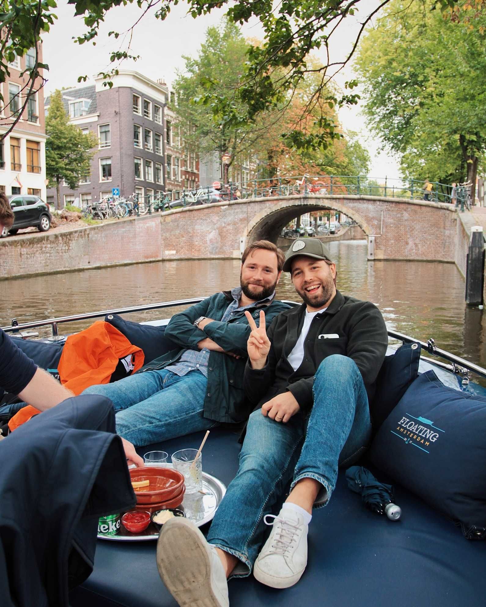 Två kollegor i en båt på en kanal i Amsterdam, den ena gör ett V-tecken