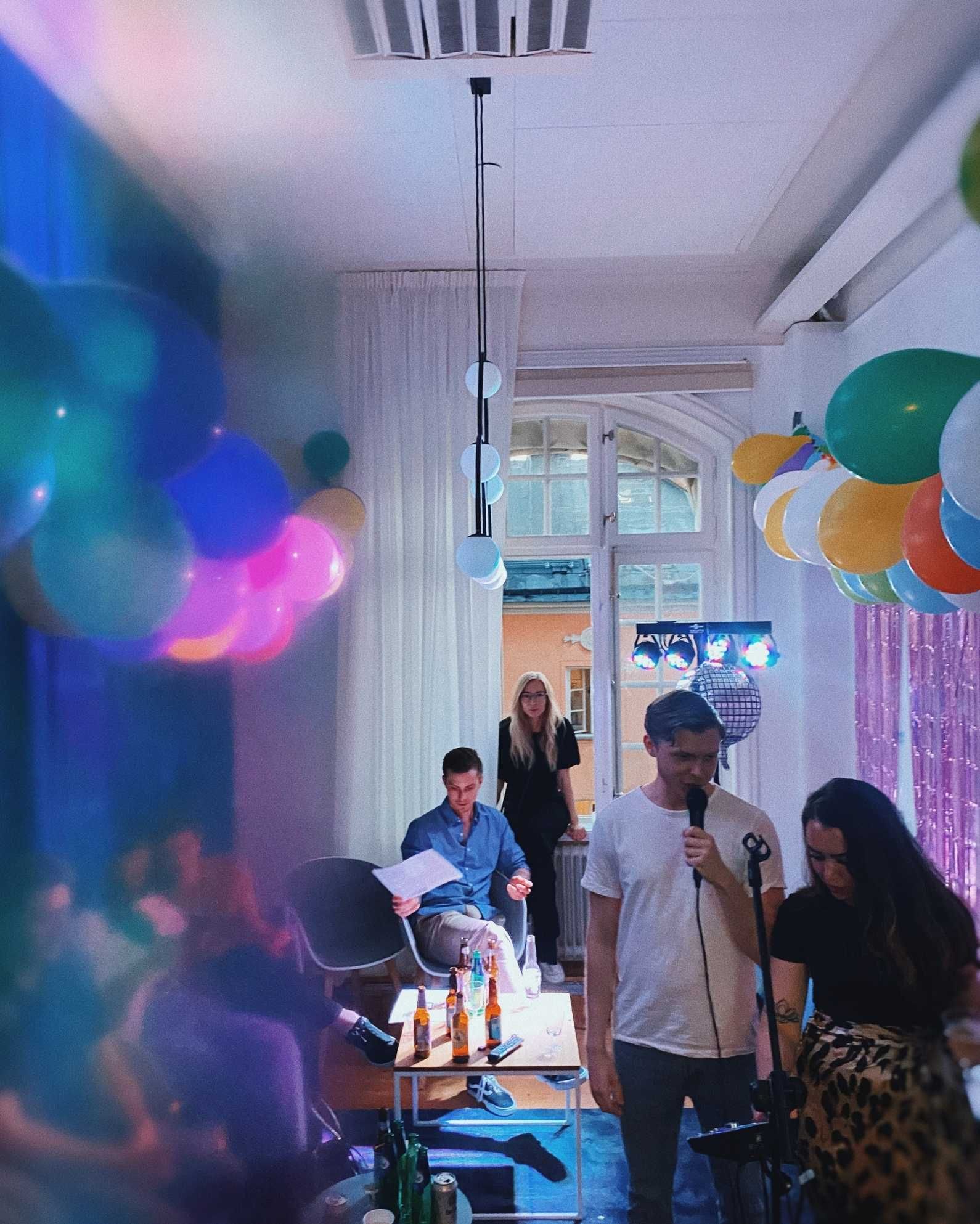 Kollega som talar i mikrofon på en fest på kontoret med ballonger